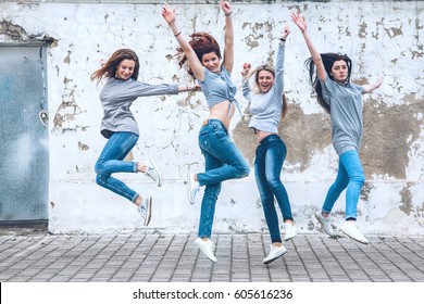 Group of four young diverse girls wearing blank gray tshirt and jeans posing against rough street wall, fashion urban clothing style, mockup for t-shirt print store
