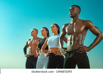 Group Of Four Young Sportsmens Women And Men, Fit Athletes Are Standing On The Sky Background Before Run. Healthy Lifestyle And Sport. Friends In Black And White Sportswear. Fitness Concept.