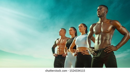 Group Of Four Young Sportsmens Women And Men, Fit Athletes Are Standing On The Sky Background Before Run. Healthy Lifestyle And Sport. Friends In Black And White Sportswear. Fitness Concept.