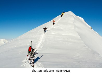 Group Of Free Riders Climbing A Mountain Peak Nearby Ski Resort Area In The French Alps, In A Clear Winter Day.