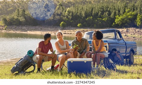 Group Of Friends With Backpacks By Pick Up Truck On Road Trip Drinking Beer From Cooler By Lake - Powered by Shutterstock