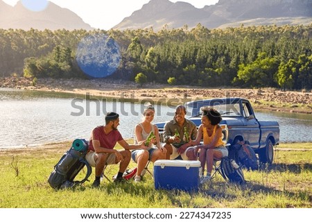 Group Of Friends With Backpacks By Pick Up Truck On Road Trip Drinking Beer From Cooler By Lake