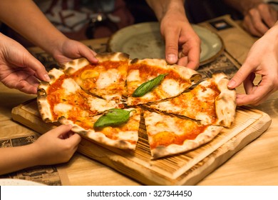 A group of friends in a cafe hands taking slices of pizza margherita - Powered by Shutterstock