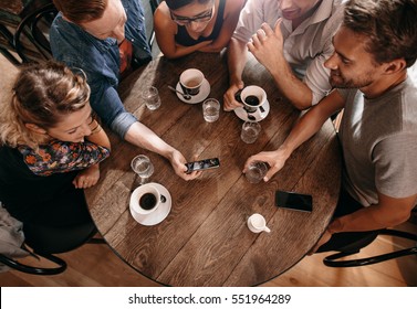 Group of friends at the cafe and looking at smart phone. Man showing something to his friends sitting by. - Powered by Shutterstock