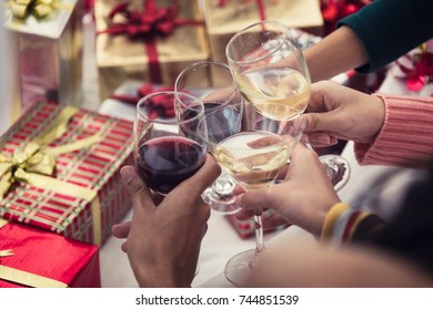 Group Of Friends Celebrating Christmas Party Dinner At Home And Caps Toasting With Alcohol Drink In Champagne Glass, Christmas Or Holiday New Year Concept And Have Gift Boxes For Background