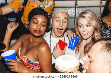 Group of friends celebrating with drinks and cake. Diverse party with young adults enjoying a festive atmosphere, holding colorful cups and a cake. Friends celebrating at birthday party. - Powered by Shutterstock