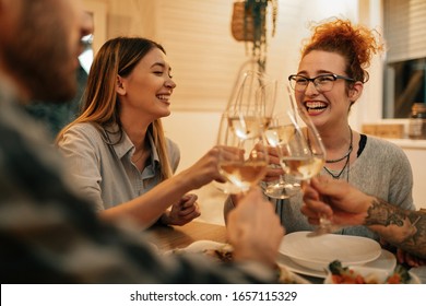 Grupo de amigos celebrando y tostando con vino durante la cena en el comedor. La atención se centra en las mujeres felices. 