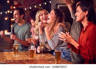 Group Of Friends Celebrating Watching Sports Game Or Match Drinking In Bar Together