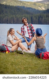A group of friends chatting while taking a rest at the lake during mountain hiking on a beautiful day. Trip, nature, hiking