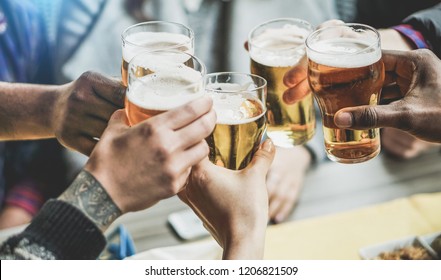 Group of friends cheering with beers in pub restaurant - Young people having fun drinking and toasting on happy hour at trendy bar - Friendship and youth concept - Focus on right black hand
