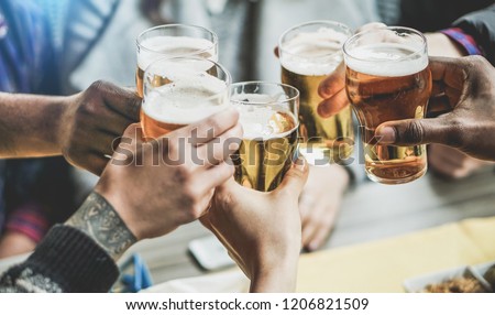 Group of friends cheering with beers in pub restaurant - Young people having fun drinking and toasting on happy hour at trendy bar - Friendship and youth concept - Focus on right black hand