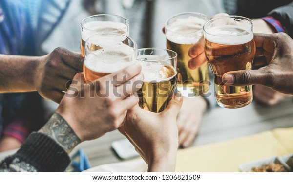 Group of friends cheering with beers in pub\
restaurant - Young people having fun drinking and toasting on happy\
hour at trendy bar - Friendship and youth concept - Focus on right\
black hand