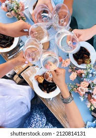 Group Of Friends Cheering With Glasses Of White Wine Above Table With Mediterranean Food Mussels While Enjoying Dinner Outdoors, People Clinking Wineglasses During Summer Picnic, View From Above