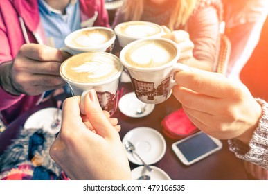 Group Of Friends Cheers With Cappuccino Cup In Cafe Bar With Phone On Table - Family Having Fun Drinking Together At Restauran In Winter Season Closeup Scene With Soft Vintage Filter And Sun Halo 