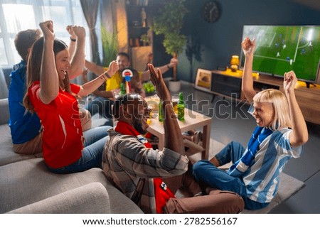 A group of friends cheers while watching a soccer match on TV. They celebrate with excitement, raising their hands and enjoying snacks and drinks in a cozy living room.