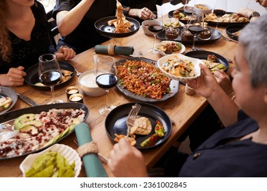 group of friends or colleagues sit around a richly set table of mediterranean food and talk and eat together in the living room or restaurant.
 - Powered by Shutterstock