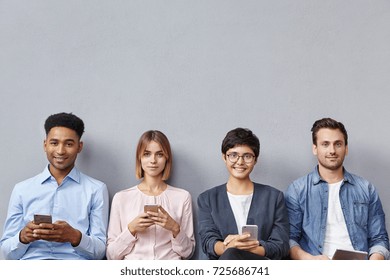Group of friends or companions, meet together to discuss merging of companies, wait for one more partner, use modern gadgets, recieve messages or download pictures, isolated over grey background - Shutterstock ID 725686741