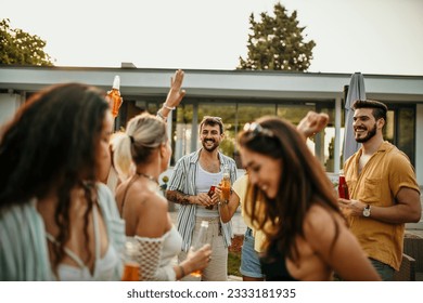 Group of friends dancing and smiling gather on the poolside, toasting with their cocktails to the beautiful colors painting the sky.	 - Powered by Shutterstock