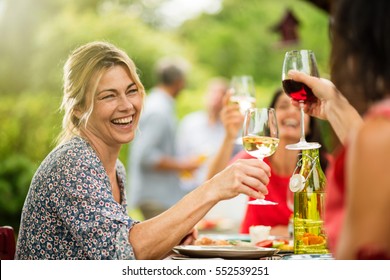 Group Of Friends Doing A Bbq, Focus On A Beautiful Woman Toasting With Her Glass Of Wine. A Beautiful Garden In The Background. Shot With Flare