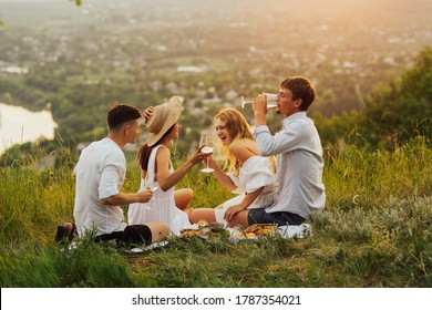 Group of friends doing summer picnic in nature. Happy people have fun, smiling and drinking white wine. Young friends on summer day are sitting on the top of mountain.  - Powered by Shutterstock