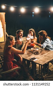 Group Of Friends Drink Beer On The Terrace And Toast During Summer Night