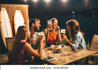 Group Of Friends Drink Beer On The Terrace And Toast During Summer Night