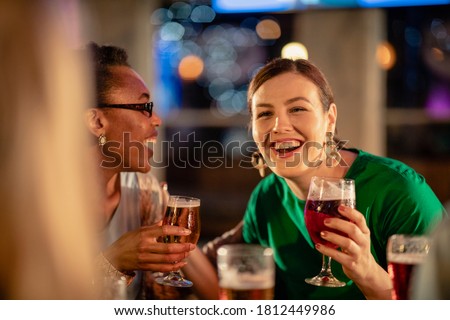 Group of friends drinking alcoholic drinks outdoors at a bar/restaurant, celebrating and having fun together.