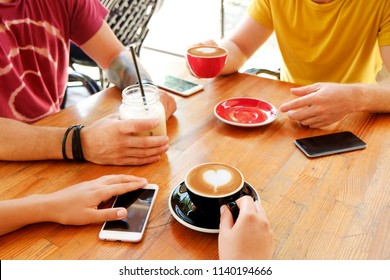 Group of friends drinking cappuccino at coffee shop, staring at smartphones, checking likes & messages. Addiction to social media. Young men & women holding cell phones & drinks. Background, top view. - Powered by Shutterstock