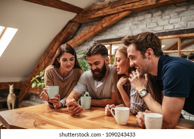 A Group Of Friends Drinking Coffee At The Apartment And Looking At Something On A Cellphone.