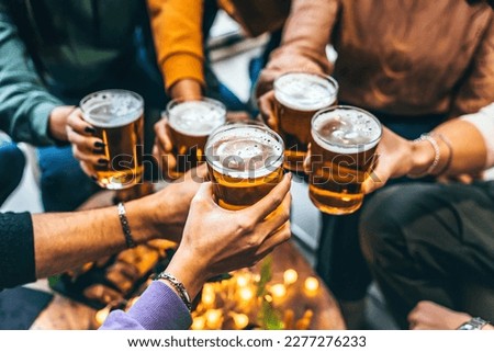 Group of friends drinking and toasting glass of beer at brewery pub restaurant- Happy multiracial people enjoying happy hour with pint sitting at bar table- Youth Food and beverage lifestyle concept
