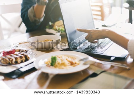Group of Friends are during meal in cafe. Crop young people sitting at restaurant using laptop computer.