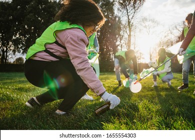 Group of friends during a volunteer garbage collection event in a park at sunset - Millennial having fun together - Happy people cleaning area with bags - Ecology concept - Powered by Shutterstock