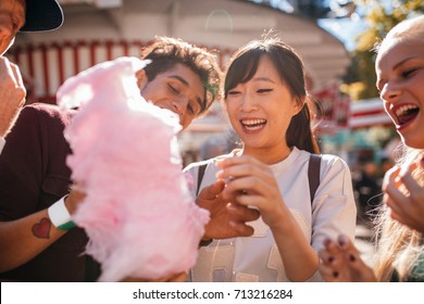 Group Of Friends Eating Candyfloss At Amusement Park. Smiling Young People Sharing Cotton Candy Outdoors.