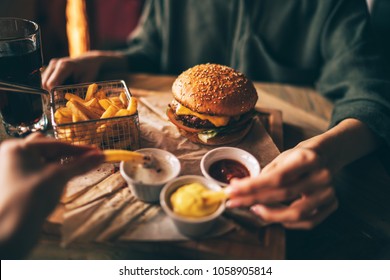 Group of friends eating at fast food. Friends are eating burgers while spending time together in cafe.Tasty grilled beef burger with lettuce and mayonnaise served on pieces of brown paper.