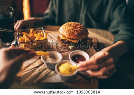 Group of friends eating at fast food. Friends are eating burgers while spending time together in cafe.Tasty grilled beef burger with lettuce and mayonnaise served on pieces of brown paper.