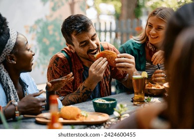 Group of friends eating Mexican food in a restaurant. Focus is on man biting a taco.