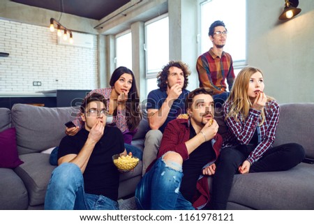 A group of friends eating pizza wathing tv in the room.