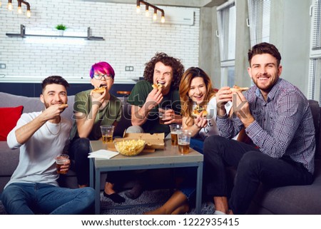 A group of friends eating pizza wathing tv sitting on the couch.