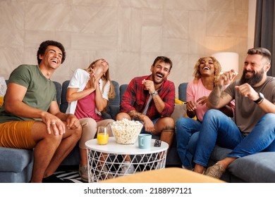 Group of friends eating popcorn and laughing while watching funny movie on TV at home
