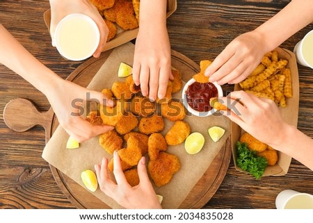 Group of friends eating tasty nuggets on wooden background