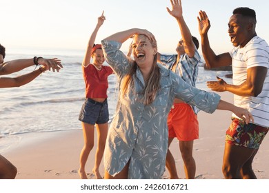 Group of friends enjoy a beach party at sunset. Young adults dance and celebrate in an outdoor coastal setting. - Powered by Shutterstock