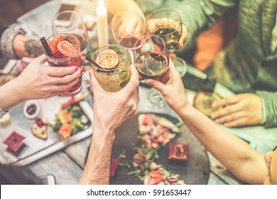 Group of friends enjoying appetizer in american bar - Young people hands cheering with wine and tropical fruits cocktails - Radial purple and green filters editing - Focus on left hands glasses