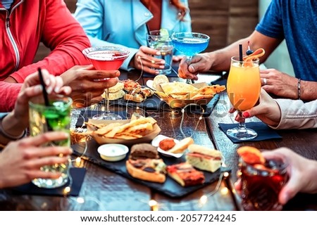 Group of friends enjoying appetizer drinking and eating in a bar - Close-up of hands of young people holding colorful cocktails in the happy hour time - Social gathering party time concept