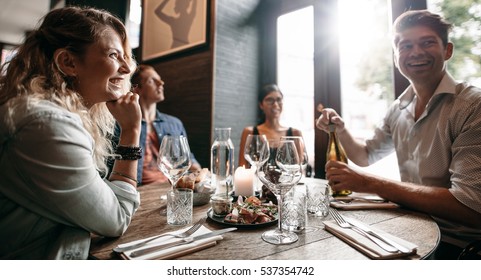 Group Of Friends Enjoying An Evening Meal With Wine At A Restaurant. Happy Young Man And Woman Having Dinner In A Restaurant.