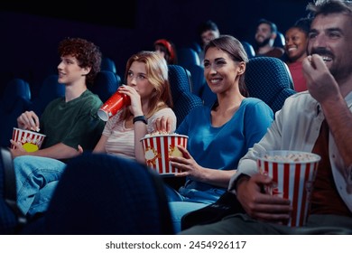 group of friends enjoying in film projection in movie theater. Focus is on woman eating popcorn.  - Powered by Shutterstock