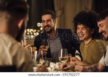 Group of friends are enjoying a meal in a restaurant. They are are talking and laughing while eating and drinking wine.