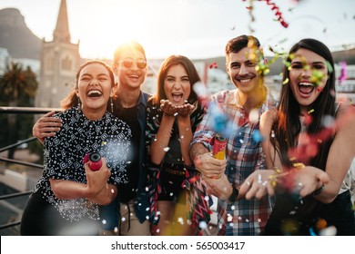 Group of friends enjoying party and throwing confetti. Friends having fun at rooftop party.