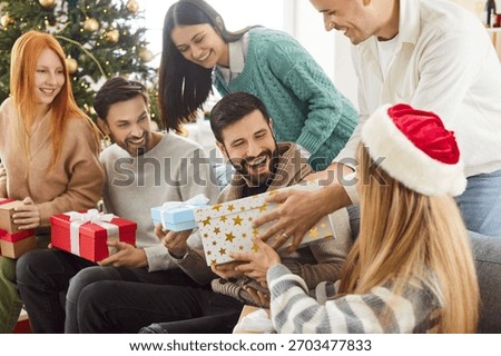 Group of friends exchanges gift boxes during a New Year or Christmas party at home. The holiday celebration creates moments of surprise, joy, and togetherness in a festive and warm atmosphere.