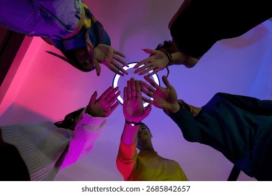 A group of friends extending their hands towards the camera with colorful ambient lighting, symbolizing connection, unity, and excitement in a spirited indoor environment.