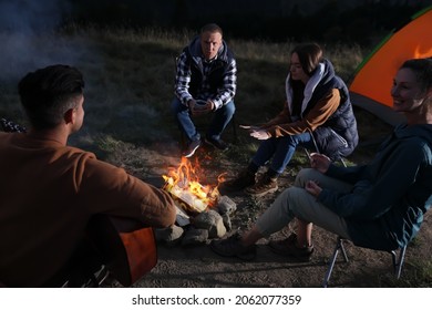 Group Of Friends Gathering Around Bonfire At Camping Site In Evening